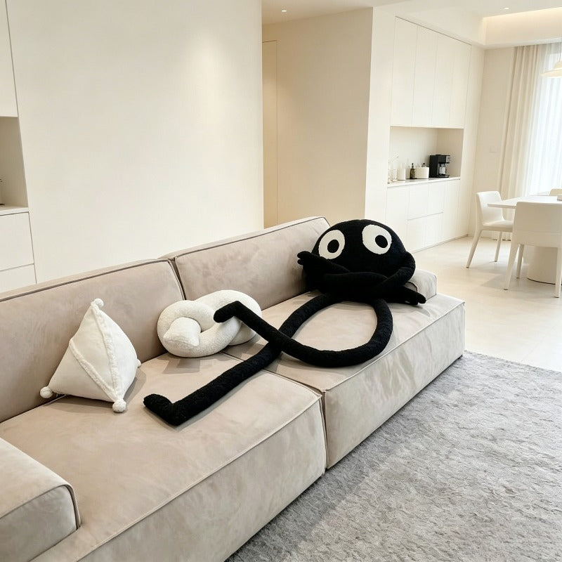 Black long-limbed googly eye plush pillow draped over a couch